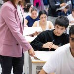 Estudiantes en aula durante un examen, con docente supervisando.