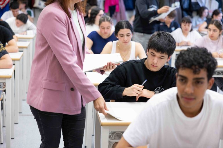 Estudiantes en aula durante un examen, con docente supervisando.