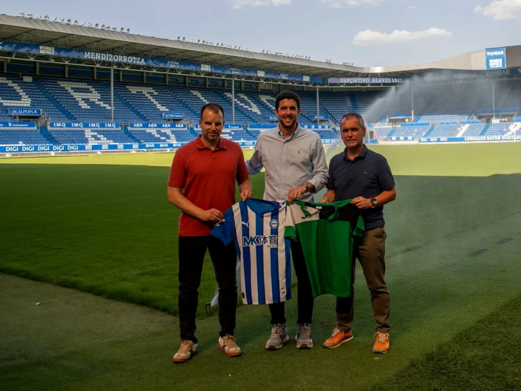 Tres personas sosteniendo camisetas en un estadio de fútbol.
