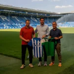 Tres personas sosteniendo camisetas en un estadio de fútbol.