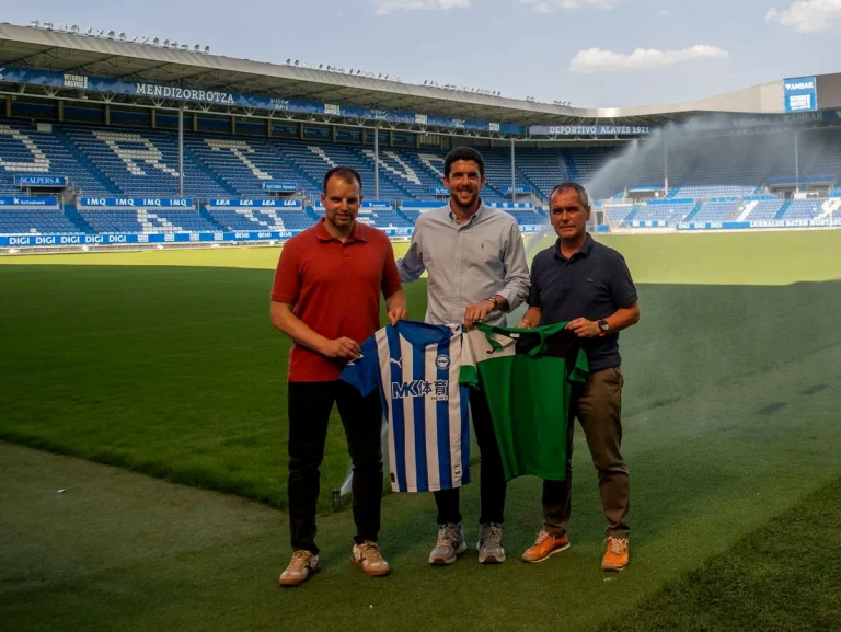 Tres personas sosteniendo camisetas en un estadio de fútbol.