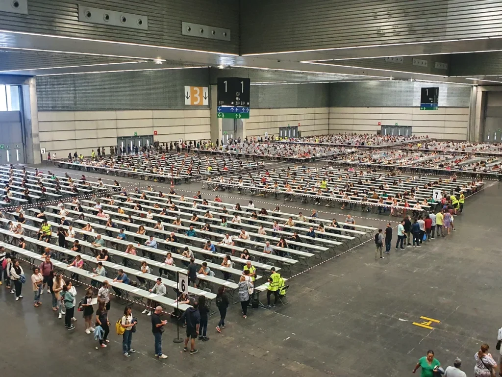 Vista general de un gran espacio con mesas y personas en fila