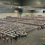 Vista general de un gran espacio con mesas y personas en fila