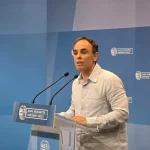 Hombre hablando en un podio con micrófonos en un evento oficial