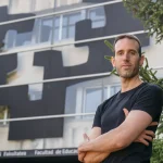 Hombre posando frente a un edificio moderno con diseño abstracto.